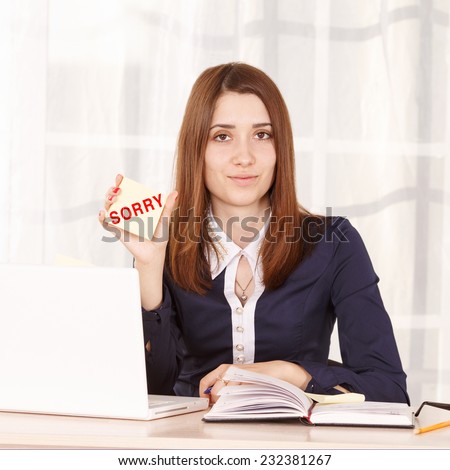Sorry. A woman employee at work in the office shows the inscription change. It is near the laptop. Girl secretary, manager sitting at the table on time of the day. Young girl student apologizes.