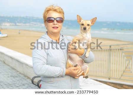 Adult woman walking with a dog on a sea beach. Walking with a pet. Dog - a friend of pensioners. Beach, sea, animals, walk, ocean, fresh air, the resort - the concept of lifestyle old woman retired.