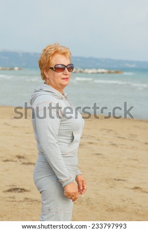 Adult woman walking on the sea beach. A walk in the fresh sea air. Sea, beach, walk, ocean, fresh air, health - concept of the modern lifestyle of the old woman on a pension. Vacation and do the walk.