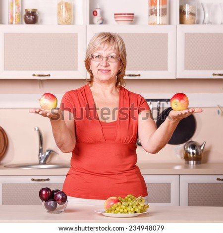 Woman preparing fruit in the kitchen. Adult woman holding fresh fruit. Happy woman holding plate full of fruits in the kitchen background. Apples, plums, grapes - kitchen stories are preparing food.
