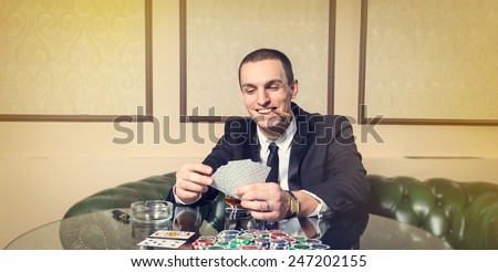 A man in a business suit sitting at the game table. Male player. Passion, cards, chips, alcohol, dice, gambling, casino - it is as male entertainment. Dangerous fun card game for money. Let the smoke.