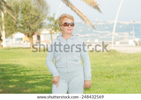 Adult woman on the background of the sea. Senior woman in tracksuit enjoying life. Fitness classes in the open air near the sea and the beach. Lifestyle adult retired. Fitness, adults, rehabilitation