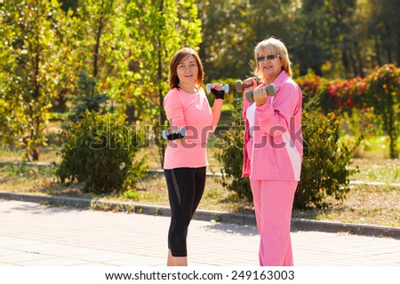 Young woman - coach with an older woman engaged in physical exercise. Take care of health at any age. Lifestyle. Adult woman and a young girl are engaged in fitness and sport together in nature.