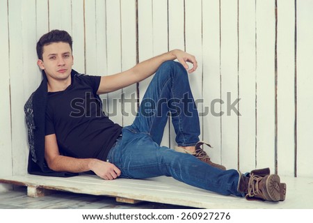 Male model posing on a light background of wood. Portrait of young beautiful fashionable man against wooden wall. Jeans fashion man with short dark hair. Wearing blue jeans, jacket.
