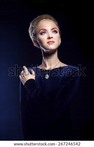 Woman in a blue dress on a background of blue blue glow of light. Beautiful noble woman of aristocratic origin. Photo portrait of a woman on a dark blue background. Woman looking at the top
