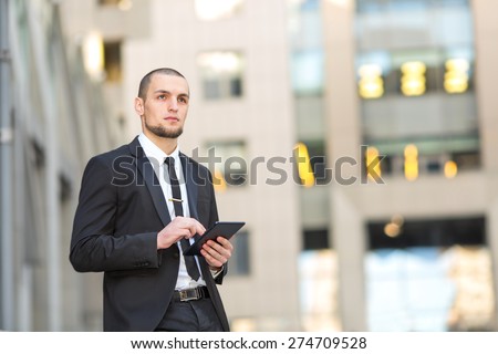 Modern businessman. Young man of arabic origin in a suit. Business man in the background office building. Confident businessman portrait. Confident, charismatic modern business man. Electronic tablet.