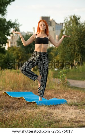 Yoga woman in city. Young and beautiful woman practices yoga in a city park on a background of buildings. Young woman doing yoga exercises outdoor.