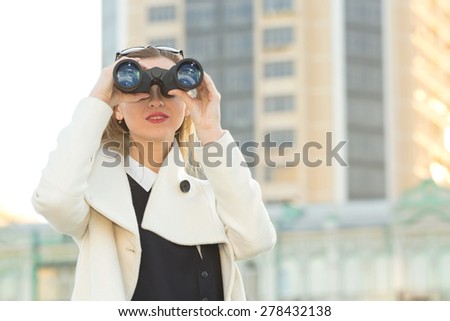 Woman and binoculars. Business woman with binoculars in his hand against the background of the streets downtown. Businesswoman holding binoculars. Concept - looking for a job. Young girl with spying.