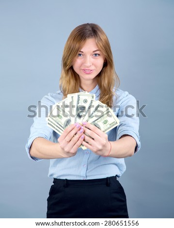 Girl student or a young business woman holding money in US dollars, on blue background. Happy female holding US dollars. Close up of young beautiful woman with us dollar money in hand, with copy space
