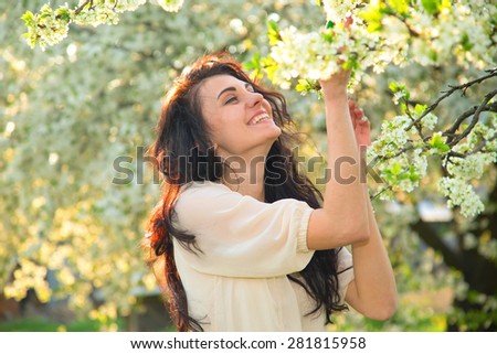 Portrait of a brunette woman inhales the scent of flowers. Happy woman enjoying the scent of blooming flowers on the tree. Young beautiful happy girl. She rests and enjoys the scent of flowers. Story.
