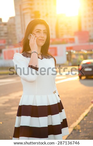 Woman talking on the mobile phone. It is against the backdrop of the city in the rays of sunset. Woman of Asian appearance is in the rays of a sunset on the background of urban buildings. Azerbaijan