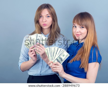 Two young women. Business emotional women hold in their hands the money, it\'s a lot of dollars. Two women earn money, they received their salary. Positive emotions for the right solution. Win lottery.