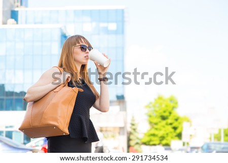 Urban woman commuter walking drinking coffee. Business woman in the city. Cheerful woman in the street drinking morning coffee. Happy young trendy woman drinking take away coffee and walking with bags