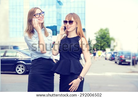 Two business women talking on mobile phone. Two young modern beautiful women. Two stylish women talking on a mobile phone. Woman on the background of the city. Happy girls student. Phone conversation