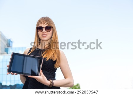 Woman showing tablet computer on business office building background. Business woman in sunglasses shows something on your plate. Display information on an electronic tablet. Demonstrating that the