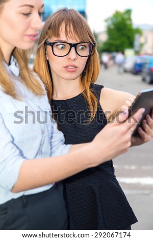 Surprise. Women using tablet. Two women using a tablet computer. Two young modern beautiful women on the background of the city street. Girls student. Two attractive women sharing ideas on a touch pad