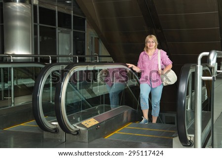 Adult woman walking on the escalator. Woman holding a big bag, carry-on baggage. Woman Trips, she goes on an escalator in the station building, an airport, a subway station. Lifted by escalators.
