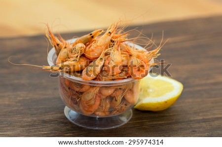 Delicious fresh cooked shrimp prepared to eat. Cooked shrimps with lemon on wooden table. Snack to beer and wine. Shrimp from the Black Sea. Serve cooked shrimp and lemon on a bar table.