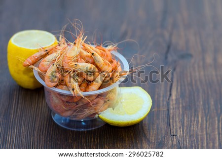Serve cooked shrimp and lemon on a bar table. Delicious fresh cooked shrimp prepared to eat. Cooked shrimps with lemon on wooden table. Snack to beer and wine. Shrimp from the Black Sea.