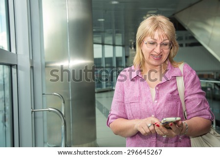 Beautiful adult woman using smart phone. Woman using app on a mobile phone. Write a message on his phone. Obtain and read the message from the phone. Woman is traveling. Bus station or airport.