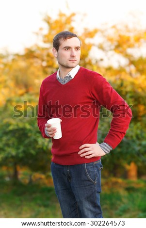 Man drinks coffee from a paper cup in the autumn park. Happiness people, drink and fast food concept - man in hat with takeaway tea or coffee cup. Calm. Drink coffee break. Street food.