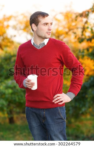 Man drinks coffee from a paper cup in the autumn park. Happiness people, drink and fast food concept - man in hat with takeaway tea or coffee cup. Calm. Drink coffee break. Street food.