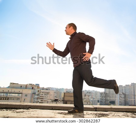 Business man running on the roof of a skyscraper on a background of blue sky.
Do warm-up exercises, or during a break. Run away from the problems and work to meet the sun and leave. Holiday break.