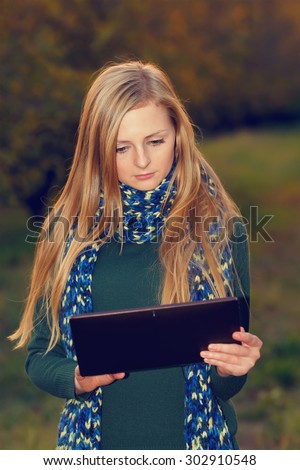 Young woman using tablet computer on autumn city park and street. Woman working on digital tablet outdoors in the park. Modern student woman using tablet pc outside on a autumn garden. Woman using pc