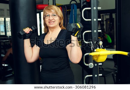 Woman holds up lifting dumbbells. Client fitness center. Woman - fitness gym. Senior exercising at gym. Old woman exercising with weights at gym.