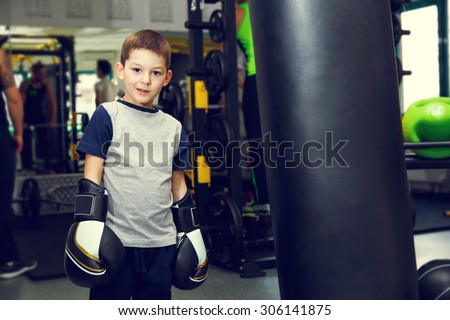 Boy with boxing gloves in the gym near the punching bag. Boy and boxing bag on gym background. Winner fight. Champion.