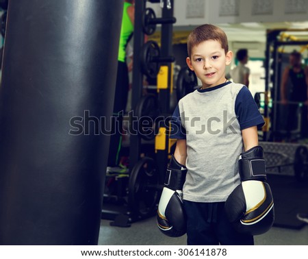 Boy with boxing gloves in the gym near the punching bag. Boy and boxing bag on gym background. Winner fight. Champion.