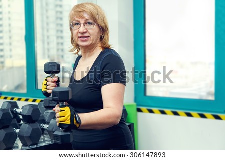 Woman holds up lifting dumbbells. Client fitness center. Woman - fitness gym. Senior exercising at gym. Old woman exercising with weights at gym. Adult woman holding dumbbell lifting up. Sport woman.