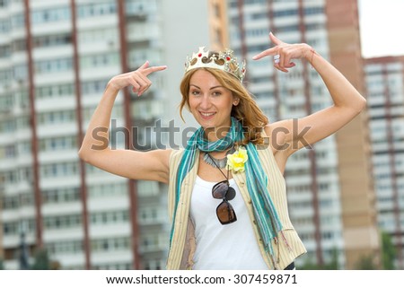 I am a woman! I am the queen! Happy emotional woman with a crown on his head against the background of the city. Woman modern Queen. A beautiful young blonde woman points to her crown on her head.