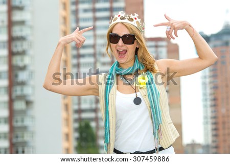 I am a woman! I am the queen! Happy emotional woman with a crown on his head against the background of the city. Woman modern Queen. A beautiful young blonde woman points to her crown on her head.