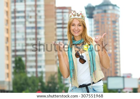 I am a woman! I am the queen! Happy emotional woman with a crown on his head against the background of the city. Woman modern queen. Beautiful young blonde woman points to her crown on her head.