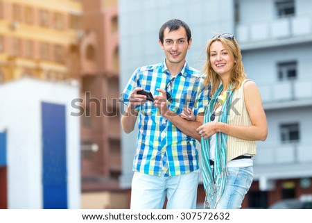 Couple man and woman informing in a smart phone on the buildings background.  Couple with smart phone. Happy young loving couple standing outdoors together and looking at the mobile phone together.