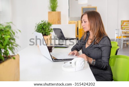 Business woman working in office. Portrait beautiful woman on the background of modern business office. Businesswoman works at a laptop at workplace. Female student in library. Green office. Lifestyle