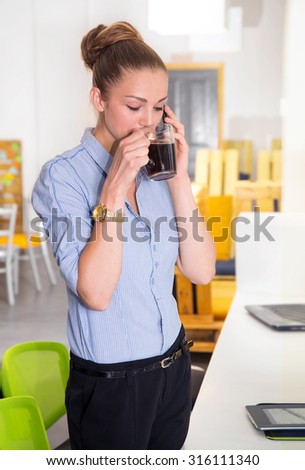 Young woman having cup of coffee in office. Coffee break. Business woman drinking from mug while working on laptop at the office. Woman at workplace. Woman on the background of modern business office.