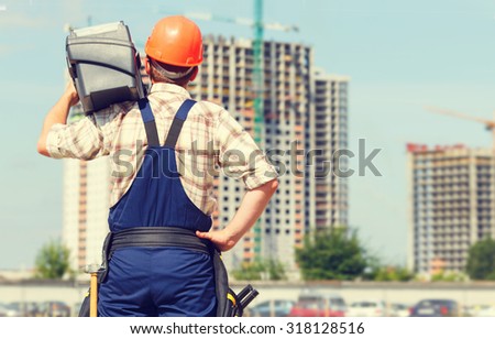 Man builder. Handyman with a tool belt. Male builder. Construction worker holding a tool box. Construction worker on a construction site. Renovation, service. Worker looking at a building site.