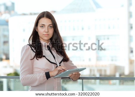 Serious business woman with tablet computer in hand on the background of building office center. Young beautiful business woman. Employee on line customer service support. Toned image.