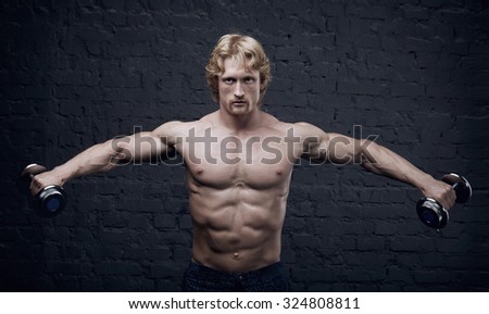 Strong man raises heavy dumbbells in his hands. He strained all the muscles of the body. Muscular man on dark background. He trains the muscles and lifts weights. Advertising fitness center or gym.