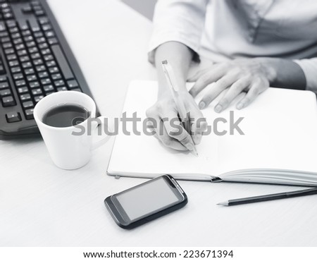 Close-up of female hands making notes in the notepad at office. Black and white image