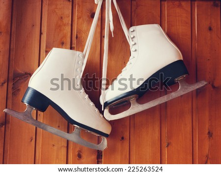 white ice skates for figure skating, hanging on a wooden background