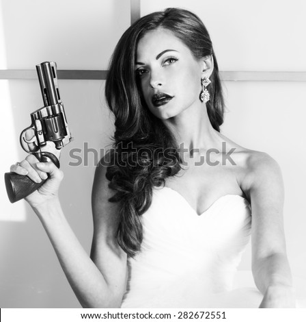 beautiful girl in a wedding dress with a gun, studio shooting. Black and white image.