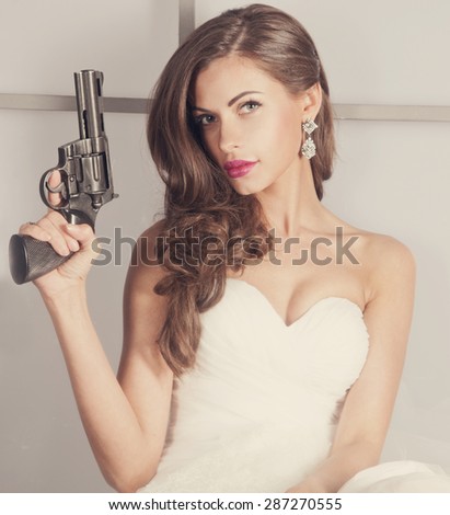 beautiful girl in a wedding dress with a gun, studio shooting