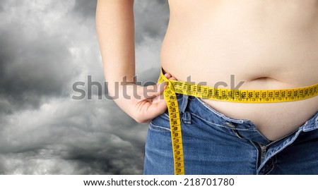 obese woman measuring her waist over a cloudy sky in the background