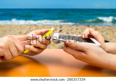 two people with the phone and connected to social networks in a beachside bar