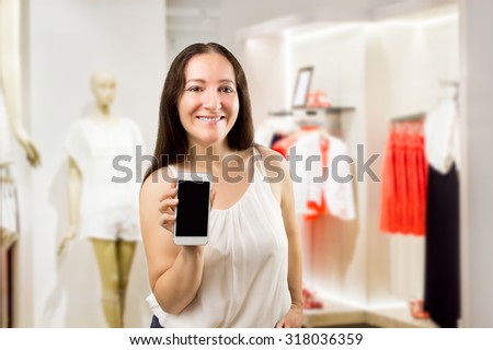 portrait of cheerful saleslady holding and showing the smartphone at the boutique