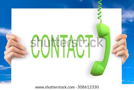 Hands holding a white board with the word contact, green vintage phone receiver hanging, blue sky background