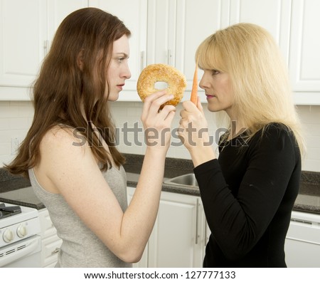 Young woman and mother argue in the kitchen over high glycemic index  bagel or  low glycemic index  (low GI food) carrot